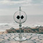 Vetrino di Helmholtz con onde sonore, oggetto scientifico decorativo, posizionato su una superficie con vista mare e case sulla spiaggia.