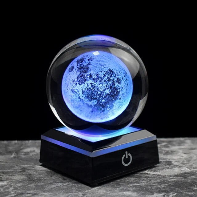 Modello di luna in cristallo illuminata con luce blu, posizionata su base nera con pulsante di accensione, perfetta come decorazione scientifica o oggetto da collezione.