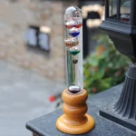 Pendolo di Newton con sfere colorate appeso a un supporto di legno, ideale come decorazione scientifica e oggetto educativo per appassionati di fisica.