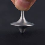 Piccola pietra di Foucault in metallo, mostrata tra le dita, evidenziando la sua forma conica e il movimento di rotazione. Perfetta come oggetto decorativo scientifico.
