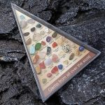 Vetrina con una collezione di gemme di pietre preziose di vari colori e tipi, etichettate con nomi scientifici, su uno sfondo di roccia nera.