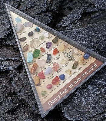 Vetrina con una collezione di gemme di pietre preziose di vari colori e tipi, etichettate con nomi scientifici, su uno sfondo di roccia nera.