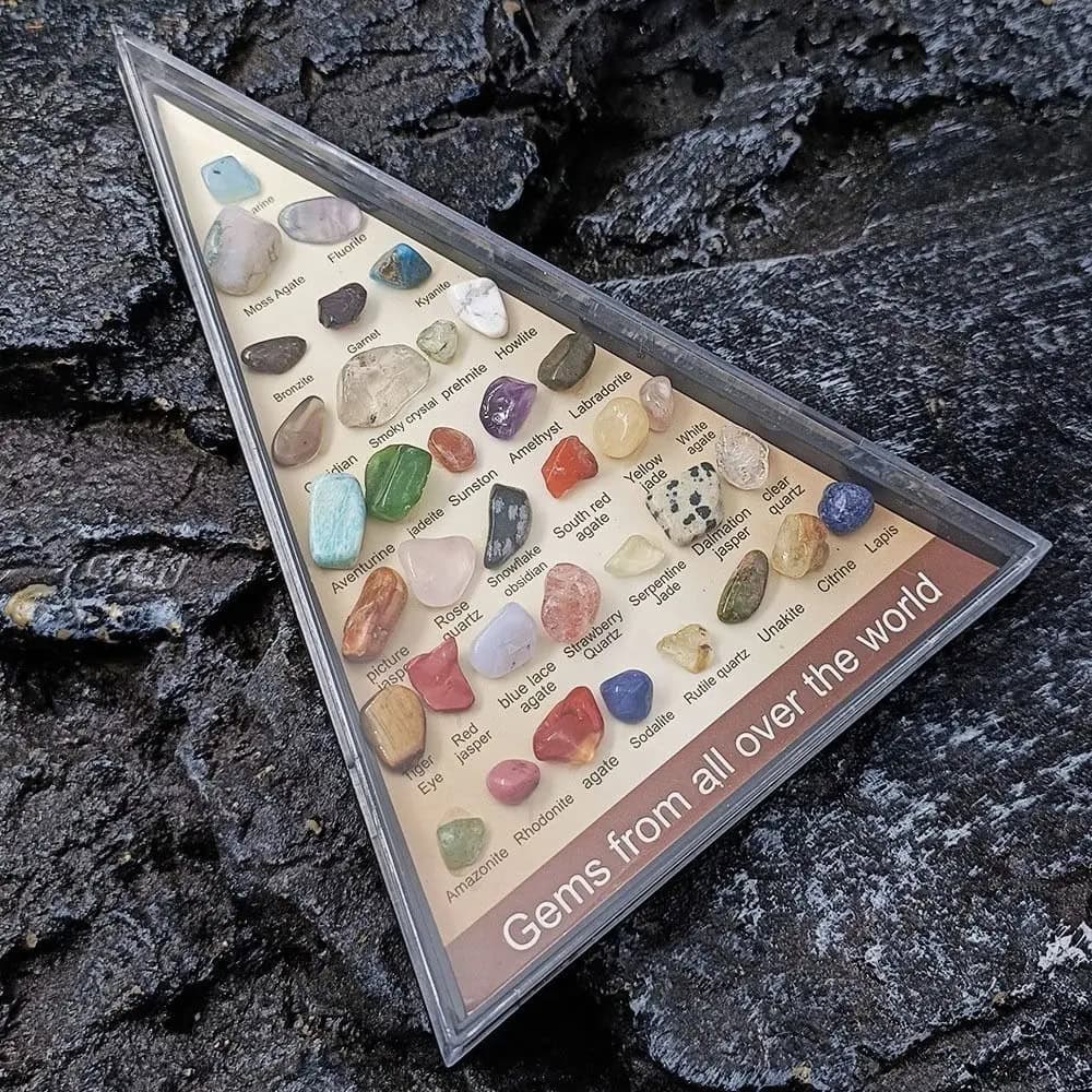 Vetrina con una collezione di gemme di pietre preziose di vari colori e tipi, etichettate con nomi scientifici, su uno sfondo di roccia nera.