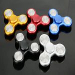 Set di cinque fidget spinner colorati in oro, rosso, blu, nero e bianco, posizionati su una superficie riflettente nera, ideali come oggetti decorativi o per alleviare lo stress.