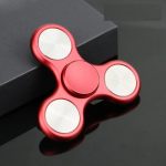 Fidget spinner rosso con tre bracci e cuscinetti metallici, oggetto antistress popolare, su sfondo scuro.