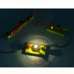 Modello di circuito elettrico con lampadina accesa, componenti colorati e collegamenti in filo, ideale per esperimenti scientifici e attività educative.