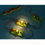Punto di partenza di un circuito elettrico con lampadine e morsetti, rappresentato con componenti colorati e fili collegati, ideale come oggetto decorativo scientifico.