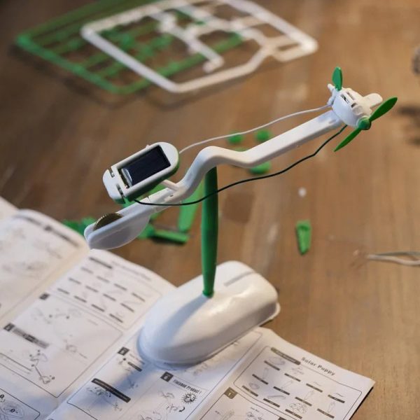Modello di drone scientifico con pannello solare e pale verdi, posizionato su un supporto, con strumenti di laboratorio e schede di istruzioni sul tavolo.