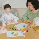 Due bambini e un'insegnante che interagiscono con modelli planetari e strumenti scientifici in un ambiente educativo, promuovendo l'apprendimento della scienza e dell'astronomia.
