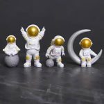 Astronauti in miniatura con caschi dorati e tute bianche, posizionati su una superficie scura, con uno seduto sulla luna e altri in piedi, creando un'atmosfera spaziale e futuristica.