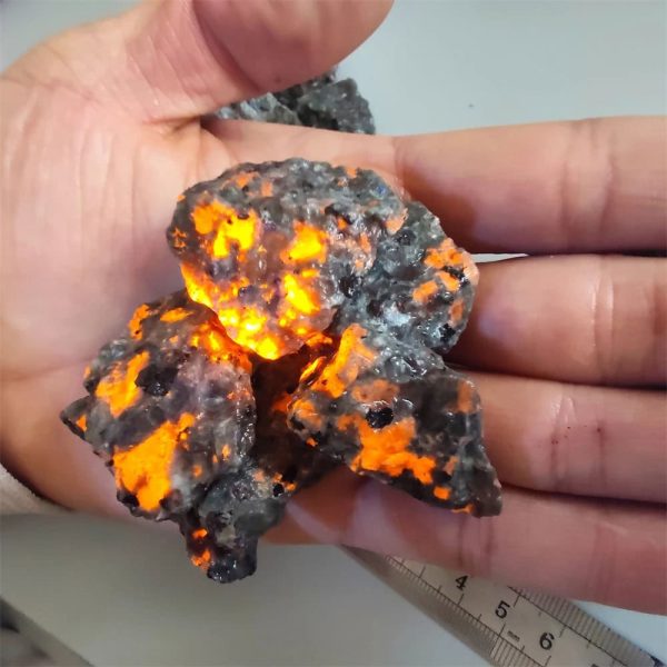 Vetro di meteorite con superficie luminosa e irregolare, che mostra un aspetto scuro con zone luminose arancioni e gialle, evidenziando le caratteristiche uniche di un frammento extraterrestre.