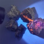 Pietre vulcaniche nere con effetti fluorescenza arancione e viola sotto luce UV, perfette come decorazioni scientifiche o oggetti da collezione.