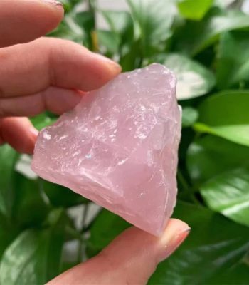 Pietra di quarzo rosa naturale, cristallo di energia positiva, usato in decorazioni e pratiche spirituali, con sfondo di foglie verdi.