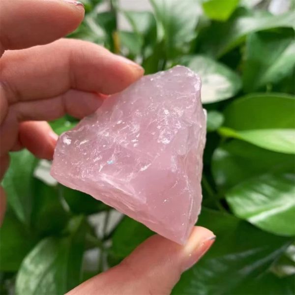 Pietra di quarzo rosa naturale, cristallo di energia positiva, usato in decorazioni e pratiche spirituali, con sfondo di foglie verdi.