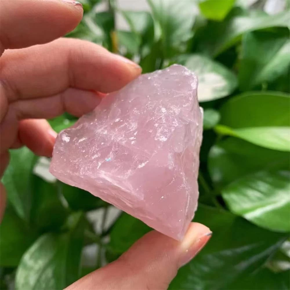 Pietra di quarzo rosa naturale, cristallo di energia positiva, usato in decorazioni e pratiche spirituali, con sfondo di foglie verdi.