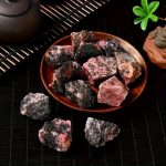 Rocce di sale rosa dell'Himalaya disposte su un piatto di ceramica, con sfondo scuro e decorazioni verdi, ideale per decorazioni scientifiche e oggetti da collezione.