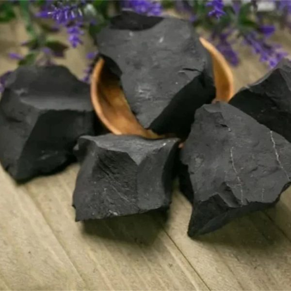 Pietre di carbonio naturale nere, perfette per decorazioni scientifiche e progetti educativi, disposte su un tavolo di legno con fiori viola sullo sfondo.