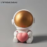Figura decorativa di un astronauta con casco dorato e corpo bianco, che tiene un cuore rosa, ideale come oggetto decorativo scientifico e per appassionati di spazio.