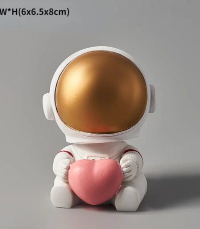 Figura decorativa di un astronauta con casco dorato e corpo bianco, che tiene un cuore rosa, ideale come oggetto decorativo scientifico e per appassionati di spazio.