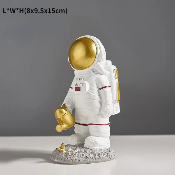 Statua decorativa di un astronauta con casco dorato, in piedi su una base che simula la superficie lunare, perfetta come oggetto di decorazione scientifica o da collezione.