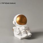 Oggetto decorativo a forma di astronauta in resina bianca con casco dorato, ideale come decorazione scientifica o da collezione. Perfetto per appassionati di spazio e scienza.