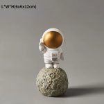 Figura di un piccolo astronauta con casco dorato, in piedi su una superficie che ricorda la luna, con dettagli realistici e stile moderno.