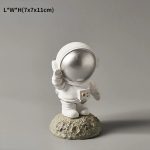 Statua di un astronauta in miniatura con casco argentato, posato su una roccia, perfetta come decorazione scientifica o da collezione.
