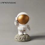 Figura di un astronauta in miniatura con casco dorato, vestito bianco, in piedi su una roccia, simbolo di esplorazione spaziale e curiosità scientifica.