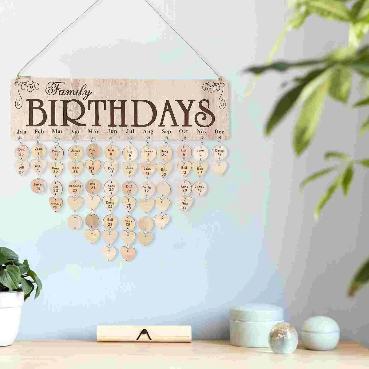 Compleanno in famiglia con decorazioni personalizzate Decorazione di compleanno familiare con un calendario di cuori in legno personalizzati con i nomi e le date di nascita, appesa a una parete con piante e oggetti decorativi.