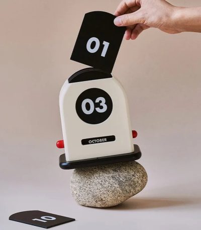Orologio flip con numeri grandi e indicatore mese ottobre, posizionato su una pietra, con numeri 01 e 03 visibili, ideale come decorazione scientifica o oggetto da collezione.