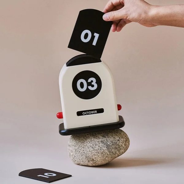 Orologio flip con numeri grandi e indicatore mese ottobre, posizionato su una pietra, con numeri 01 e 03 visibili, ideale come decorazione scientifica o oggetto da collezione.
