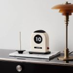 Orologio da tavolo con display digitale e design vintage, posizionato su una superficie con libri e una lampada da tavolo in stile industriale. Perfetto come decorazione scientifica e oggetto di desig.