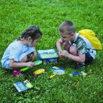 Due bambini che giocano con strumenti scientifici e kit di esplorazione all'aperto su un prato verde.