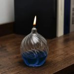 Vaso di vetro decorativo con liquido blu e fiamma accesa, oggetto scientifico e decorativo.