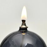 Immagine di una candela accesa con fiamma viva, posizionata su un oggetto scientifico nero, simbolo di illuminazione e scoperta.