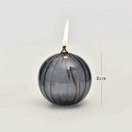 Oggetto decorativo a forma di pallina con candela accesa, altezza di circa 8 cm, in vetro trasparente con riflessi scuri, ideale come decorazione scientifica o da tavolo.