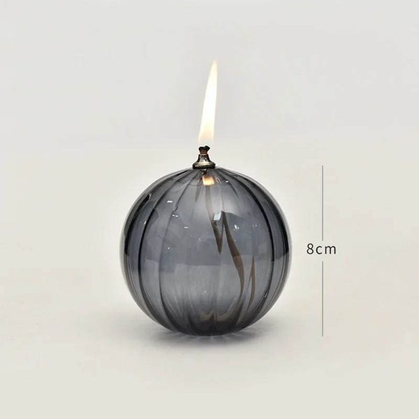 Oggetto decorativo a forma di pallina con candela accesa, altezza di circa 8 cm, in vetro trasparente con riflessi scuri, ideale come decorazione scientifica o da tavolo.