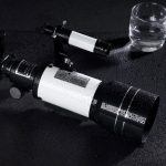 Telescopio astronomico nero e bianco con gocce d'acqua sulla superficie, posizionato su uno sfondo scuro, pronto per l'osservazione celeste.