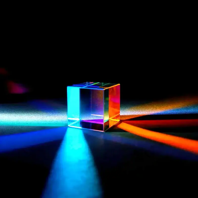 Cubo di vetro trasparente illuminato con luci colorate, crea effetti di rifrazione e riflesso su superficie scura. Decorazione scientifica ideale per ambienti moderni e studi.