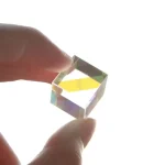 Piccolo vetro ottico trasparente con riflessi iridescenti, tenuto tra le dita, che mostra effetti di luce e colore.