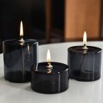 Tre candele scientifiche in vetro nero con fiamme accese, create per decorazioni e ambienti eleganti, ispirate al mondo della scienza.