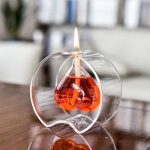 Vaso di vetro trasparente con candela accesa a forma di goccia di liquido rosso, decorazione scientifica elegante e moderna.