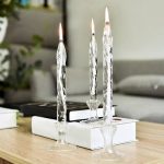 Tre candele in cristallo con fiamme accese, posizionate su una superficie di legno con sfondo di soggiorno moderno. Perfette come decorazione scientifica o ambientazione elegante.