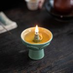 Candela in ceramica con fiamma accesa su supporto decorativo verde, atmosfera calda e accogliente.