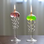 Due candele scientifiche decorative con base in vetro, una rosa e una verde, con fiamme accese, ideali come oggetti decorativi e per ambienti a tema scientifico.