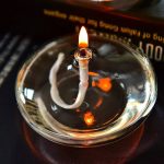 Candela scientifica accesa in un contenitore di vetro, con fiamma viva e riflessi luminosi, ideale come decorazione per ambienti scientifici o studi di laboratorio.