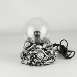Lampada decorativa con base di teschi e ossa in stile gotico, con lampadina a sfera trasparente, perfetta come oggetto di decorazione scientifica o artistica.