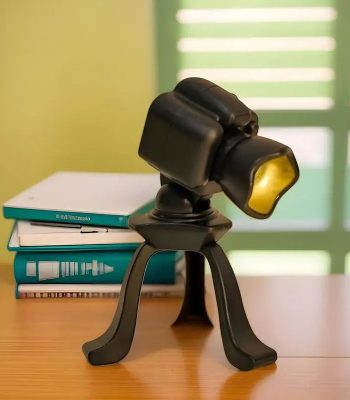 Microscopio da tavolo con supporto nero, ideale per studi scientifici e osservazioni dettagliate, posizionato su un tavolo con libri e sfondo luminoso.