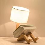 Lampada decorativa con base in legno a forma di figura umana che legge un libro, combinando funzionalità e design originale. Perfetta per ambienti moderni e studi, aggiunge un tocco di creatività e ca.