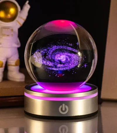 Palla di cristallo con rappresentazione di una galassia luminosa e colorata, posizionata su base con pulsante di accensione. Decorazione scientifica affascinante e moderna.